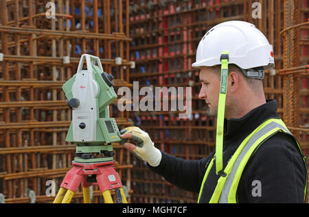 Una costruzione geometra aggiusta un livello elettronico su un grande Londra sito in costruzione. Mostra in acciaio maglia di rinforzo in background. Foto Stock