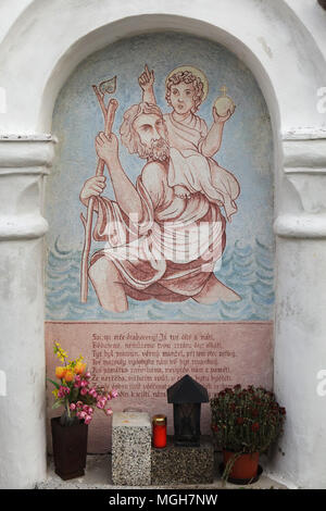 Saint Christopher portante il Cristo Bambino. Pittura murale nella cappella funebre al cimitero del villaggio in Albrechtice nad Vltavou nella regione della Boemia del Sud, Repubblica Ceca. Funerale cappelle poste sul muro del cimitero erano decorati con pitture murali nel 1840s del pittore locale František Mikule condotte con il parroco Vít Cíza, che compose anche poesie per ogni murale. I murales sono stati ridipinti diverse volte durante il XIX e XX secolo e completamente restaurato dal team guidato da Jitka Musilová nel 2010-2013. Foto Stock