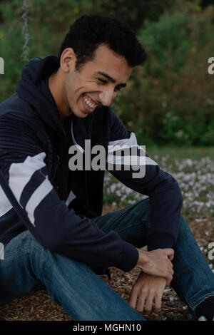 Giovane e moderno alla moda medio orientale indiano maschio modello ridendo e in posa di natura presso il parco per ritratto scatti della testa Foto Stock