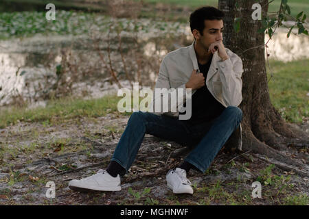 Giovane e moderno alla moda medio orientale indiano maschio modello ridendo e in posa di natura presso il parco per ritratto scatti della testa Foto Stock