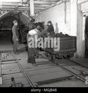 Degli anni Cinquanta, storica miniera di carbone, miniera di lavoratori in una grande area aperta vicino al pit-testa con uno scoperto di merci ferroviarie carro riempito di carbone, Inghilterra, Regno Unito. Foto Stock