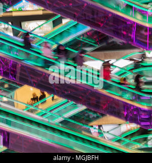 Abstract immagine sfocata del moderno centro commerciale, irriconoscibile sagome di persone sulle scale mobili e brillante retroilluminazione vivaci , background moderno per des Foto Stock
