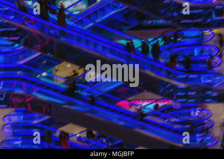 Abstract immagine sfocata del moderno centro commerciale, irriconoscibile sagome di persone sulle scale mobili, luminose brillanti retroilluminazione a led , background moderno per Foto Stock