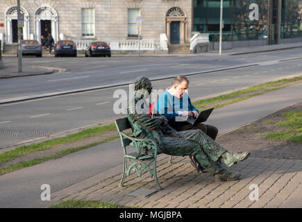 L'uomo lavora all'aperto sul banco di lavoro con computer portatile accanto alla statua del poeta irlandese Patrick Kavanagh a Dublino, Irlanda. Foto Stock