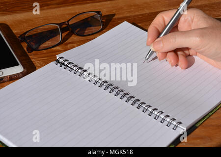 Donna con la penna in mano, pronta a scrivere in una rilegatura a spirale notebook Foto Stock