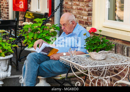 Un anziano uomo è la lettura del suo libro di fronte a una casa Foto Stock