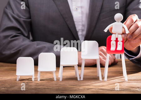 Close-up di un imprenditore la mano collocando una figura umana sulla sedia rossa sulla scrivania in legno Foto Stock