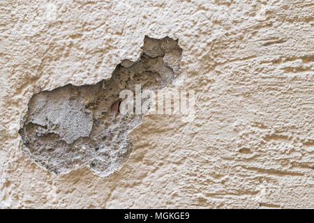 Un danneggiamento del muro di casa e fiocchi di intonaco esterno con un grande foro Foto Stock