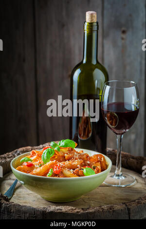 Deliziosa penne bolognese servita con un bicchiere di vino rosso Foto Stock