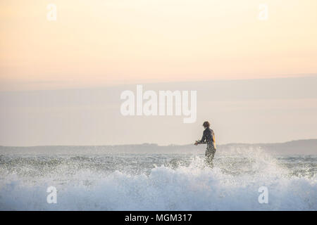 18 Aprile,2018.Tenby Uk.Surfer sulla costa britannica durante il tramonto battendo le mani.bella cielo nebuloso e dagli spruzzi delle onde.Natura e uomo.il tranquility. Foto Stock