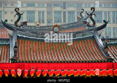 Vista frontale del famoso centro buddista cinese o il Tempio Taoista tetto con sculture ornamentali e lanterne rosse sotto la pioggia nel centro cittadino di Singapore Foto Stock