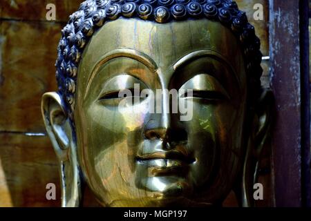 Close up di ottone statua di Buddha che mostra la faccia con espressione serena e ricco di sfumature metalliche e le texture Foto Stock