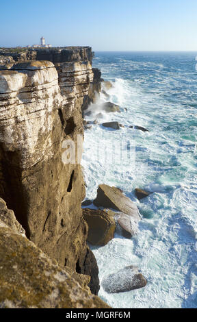 Rocce e onde di navigare nell'oceano vicino Cabo Carvoeiro (capo di carbone), Peniche penisola con faro su sfondo, Portogallo Foto Stock