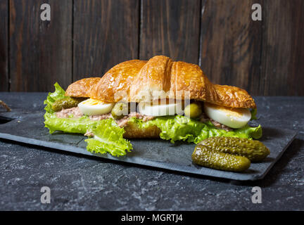 Croissant sandwich con tonno, uovo sodo, insalata e il cetriolo sul tavolo di pietra. Foto Stock