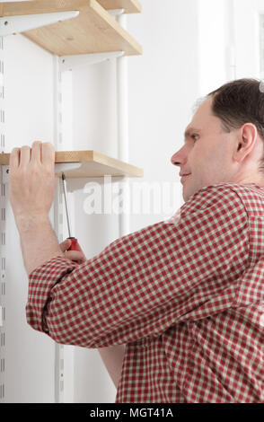 L'uomo installazione di scaffalature in legno su staffe Foto Stock