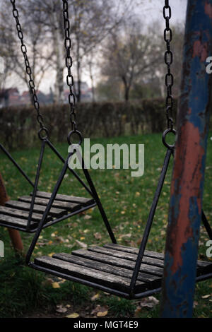 Swing deserta nel parco giochi per bambini in autunno Foto Stock