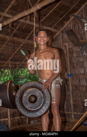 Un Palaw'ano l'uomo gioca un Philippine Agung gong con un lanciapaglia (betay) presso il villaggio tribale in Puerto Princesa, PALAWAN FILIPPINE. Foto Stock