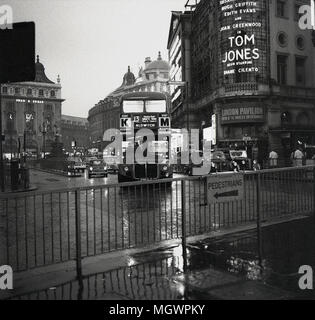 1963, immagine storica, Piccadilly Circus, Westminster, Londra, Inghilterra, su un umido umido di prima sera, un autobus routemaster sul raccordo stradale insieme ad altri mezzi di trasporto che arrivano da Regent Street. Un cartellone pubblicitario per il film, 'Tom Jones', si può vedere sulla destra della foto. Una commedia britannica, il film, un adattamento del romanzo di Henry Fielding del 1749, interpretato da Albert Figney, è stato sia un box Office che un successo critico. Foto Stock