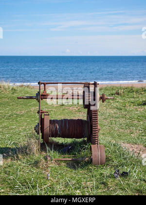 Un vecchio arrugginendo barca manuale argano utilizzato per il trasporto in barche da pesca giace abbandonata sulla banca erbosa dietro alla spiaggia in Easthaven, Scozia. Foto Stock