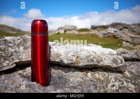 Un rosso beuta da vuoto per bevande calde poggia su un ripiano di pietra calcarea con erba verde e blu cielo dietro Foto Stock