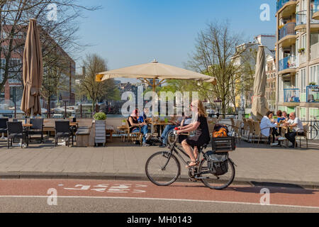 Ciclista velocità da patroni in corrispondenza di una piccola caffetteria che si affaccia su uno dei canali di Amsterdam su una bella mattina di primavera. Non ci sono più le biciclette in Amster Foto Stock