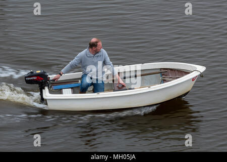 Un uomo con una piccola barca a remi o bando di gara per uno yacht con un motore fuoribordo essendo usati per guidare l'imbarcazione. Un uomo di mezza età in una piccola barca helming. Foto Stock