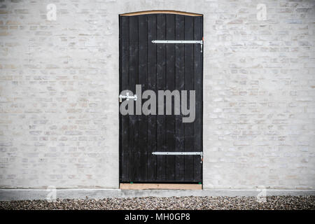 Nero porta di legno sul grigio di un muro di mattoni su una facciata esterna Foto Stock