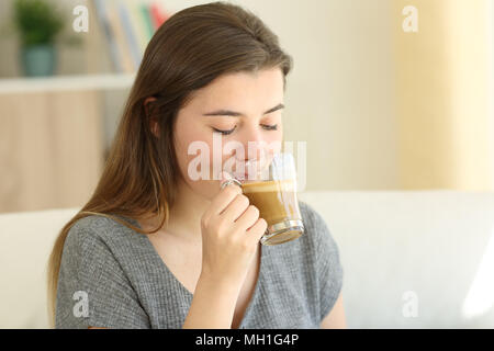 Teen di bere il caffè con il latte seduta su un divano nel salotto di casa Foto Stock