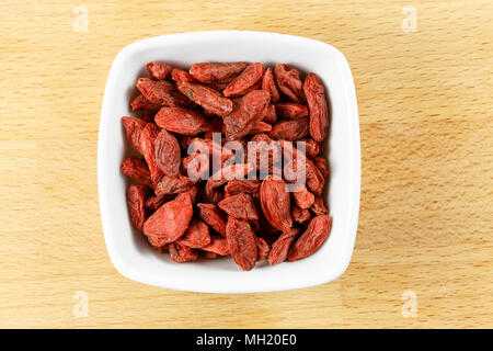Essiccati goji bacche in un recipiente su un tagliere di legno. Foto Stock