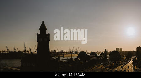 Silhouette di famosi hamburger Landungsbruecken con porto commerciale e il fiume Elba con sole serale, St. Pauli district, Amburgo, Germania Foto Stock