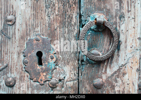 Close-up di un frammento della vecchia porta di legno con keyhole ossidato rivetti forgiato in acciaio e respingente. Texture di legno antico e dettaglio della porta. Foto Stock