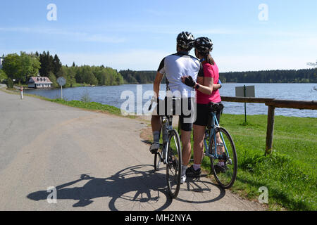 Coppia giovane in amore con la Bicicletta Equitazione durante la splendida giornata di primavera e guardando il lago azzurro Foto Stock