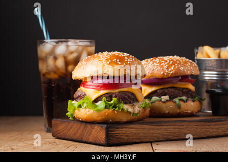 Close-up di freschi e deliziosi fatti in casa burger con lattuga, formaggio, cipolla e pomodoro su un rustico di legno. Anche le patatine fritte e Cola con ghiaccio su un di legno Foto Stock