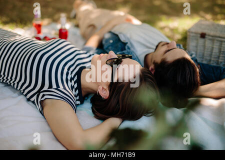 Bella donna che indossa gli occhiali da sole sdraiati su una coperta con il suo fidanzato. Paio di relax presso un parco durante un picnic. Foto Stock