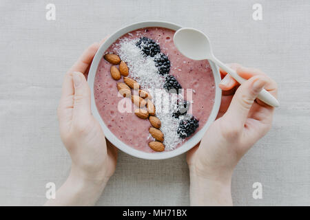 Colpo di raccolto dal di sopra della persona con ciotola smoothie guarnita con mandorle e Berry. Foto Stock