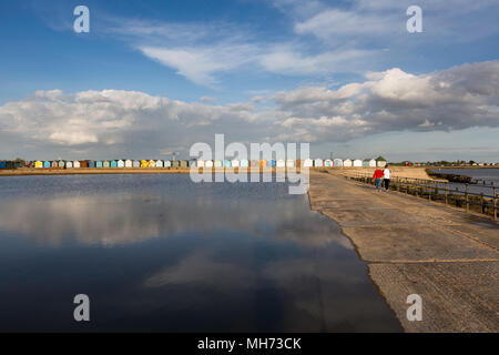 Un paio di passi accanto alla piscina di marea a Brightlingsea, Essex, Regno Unito. La pittoresca spiaggia di capanne, cielo blu e nuvole sono riflessi nell'acqua. Foto Stock