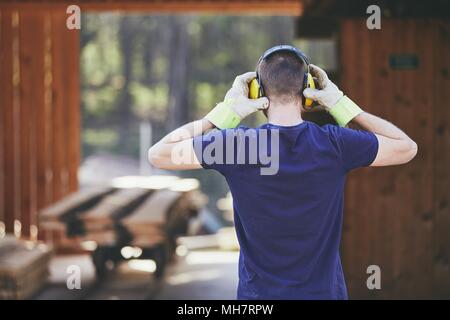 Uomo che lavora in segheria. Vista posteriore del lavoratore con auricolare. Foto Stock