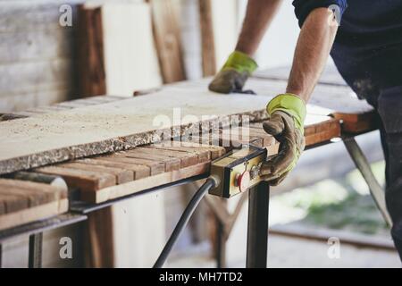 Uomo che lavora in segheria. Le mani del lavoratore con guanti di protezione. Foto Stock