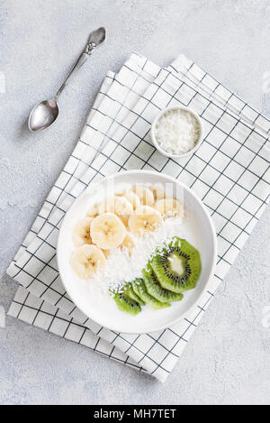 Paleo yogurt ciotola con banana, kiwi e scaglie di cocco. Una sana prima colazione, snack sani o per i pasti dei bambini. Lo yogurt naturale con frutta tropicale. Vista superiore Foto Stock