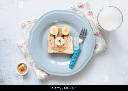 Banana burro di arachidi toast sulla piastra blu, pasto per bambini. Carino divertente orso animale a forma di pane tostato con il dado burro e banana. Pranzo a scuola per i bambini. Guarire Foto Stock