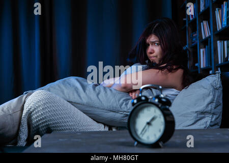 Ritratto di insoddisfatto ragazza con insonnia seduta sul letto accanto alla sveglia di notte Foto Stock