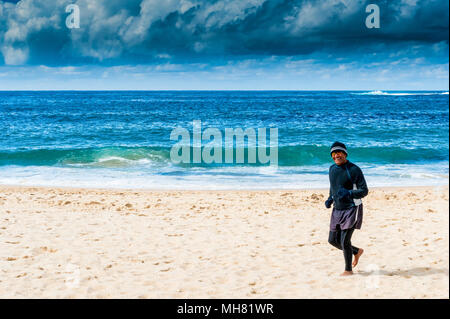 Un pareggiatore fa il suo modo lungo la famosa spiaggia Bondi, Sydney Australia, con un tempestoso cielo molto nuvoloso in background. Foto Stock