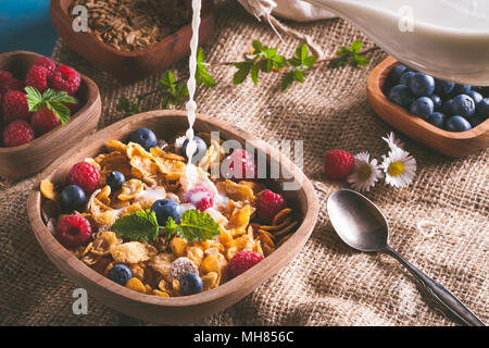 Fiocchi di mais e altri cereali con frutta fresca di lamponi mirtilli e versare il latte in una sana prima colazione. Foto Stock