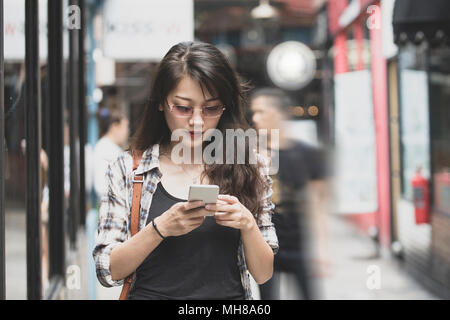 Bella donna asiatica camminando sulla strada urbana e di connessione sul telefono intelligente Foto Stock
