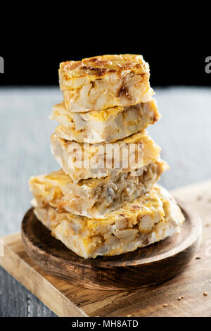 Alcuni pezzi di tipico la tortilla de patatas, frittata spagnola, su una tavola in legno rustico, contro uno sfondo nero Foto Stock