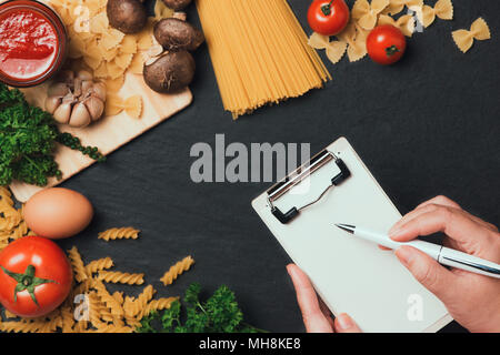 Italiano Foto di spaghetti ricetta. Mano con la scrittura della penna su carta bianca sul tavolo di cucina circondato con prodotti. Foto Stock