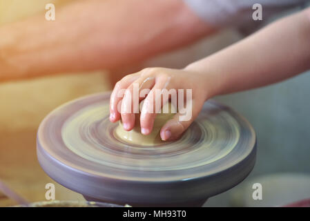 Creazione di un vaso o in un vaso di argilla bianca di close-up. Kid mani, ceramiche, officina, arte ceramica concetto. Twisted tornio del vasaio Foto Stock
