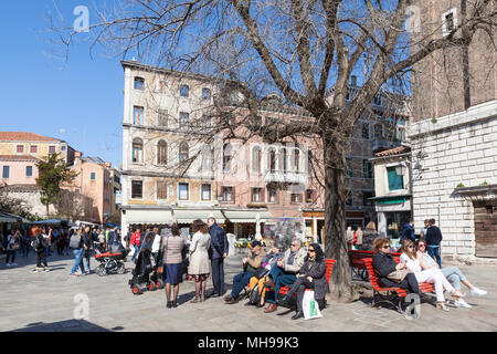 Veneziano la vita quotidiana con la gente del luogo rilassante in Campo Santi Apostoli, Cannaregio, Venezia, Veneto, Italia sulle panchine sotto un albero di sole in early spri Foto Stock