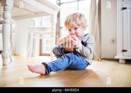 Un bimbo piccolo ragazzo seduto sul pavimento a casa. Foto Stock