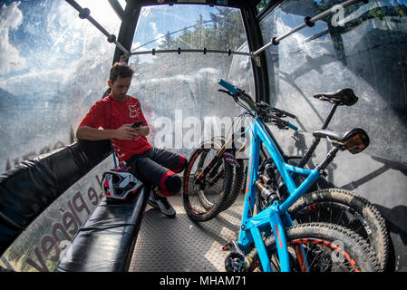 Un mountain biker siede in Le Pleney funivia con la bici in estate francesi nella città alpina di Morzine. Foto Stock